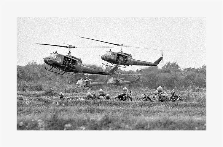 A black and white photo of two helicopters flying over soldiers.