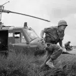 A soldier is running near an army helicopter.